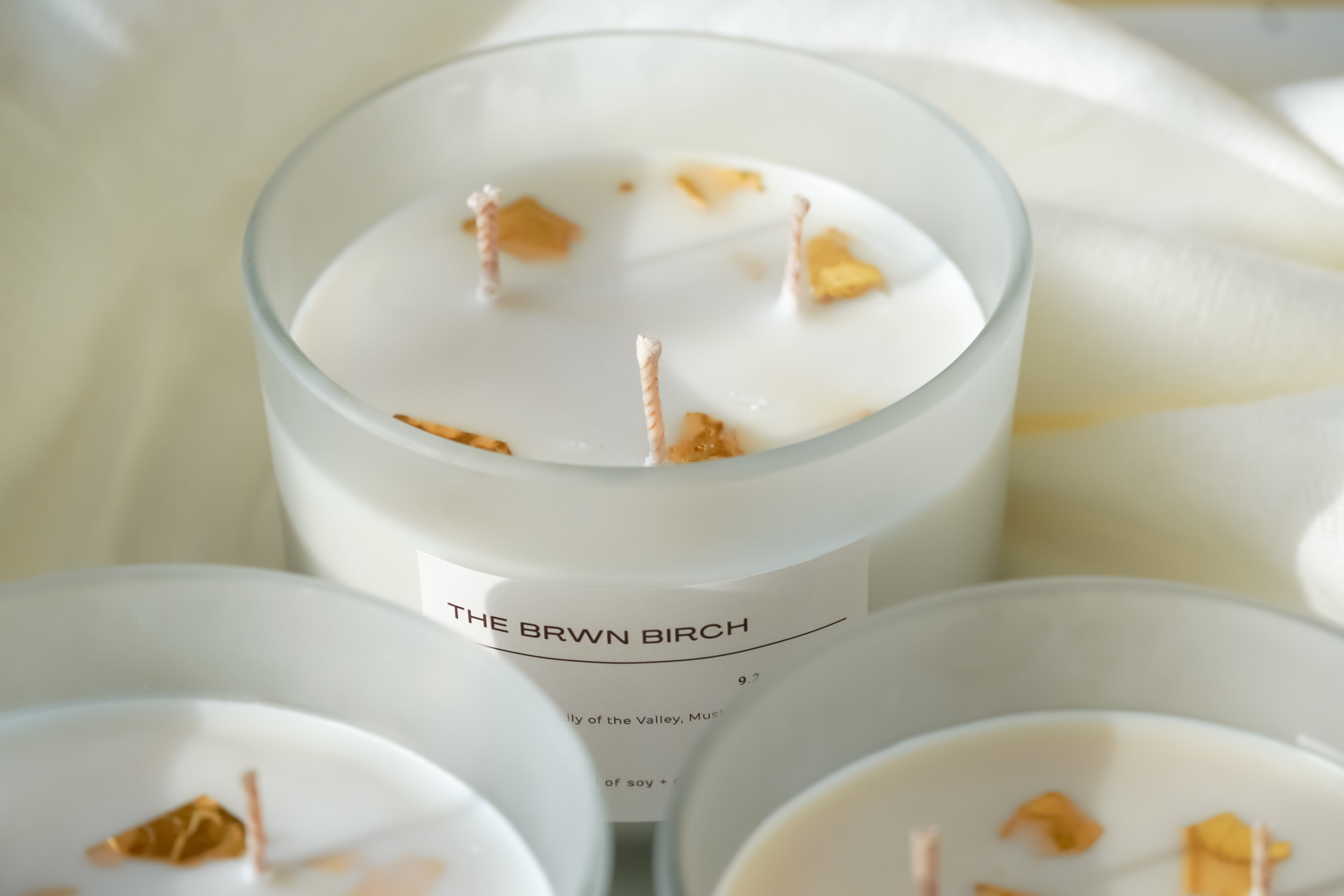 Detailed view of THE BRWN BIRCH premium 3-wick jar candle, showcasing natural soy + coconut wax topped with signature gold flakes for an intentional scent experience